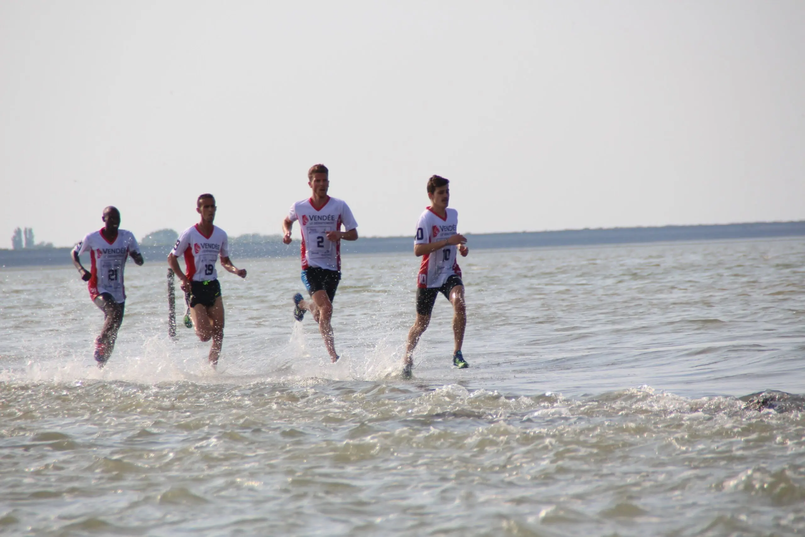 quatre coureurs en maillot vendéen courent dans l'eau de la baie