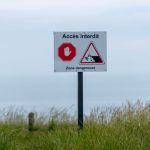 Sign saying 'Accès Interdit' in a grassy area, warning of a dangerous zone.