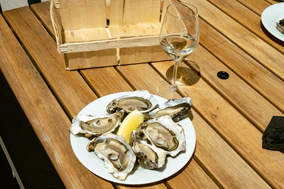 Plate of fresh oysters with a lemon wedge and wine glass on a wooden table outdoors.