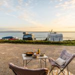 Campervans parked by the sea with outdoor dining setup