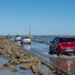 Vehicles driving on the tidal road in Beauvoir-sur-Mer, France during a sunny day.