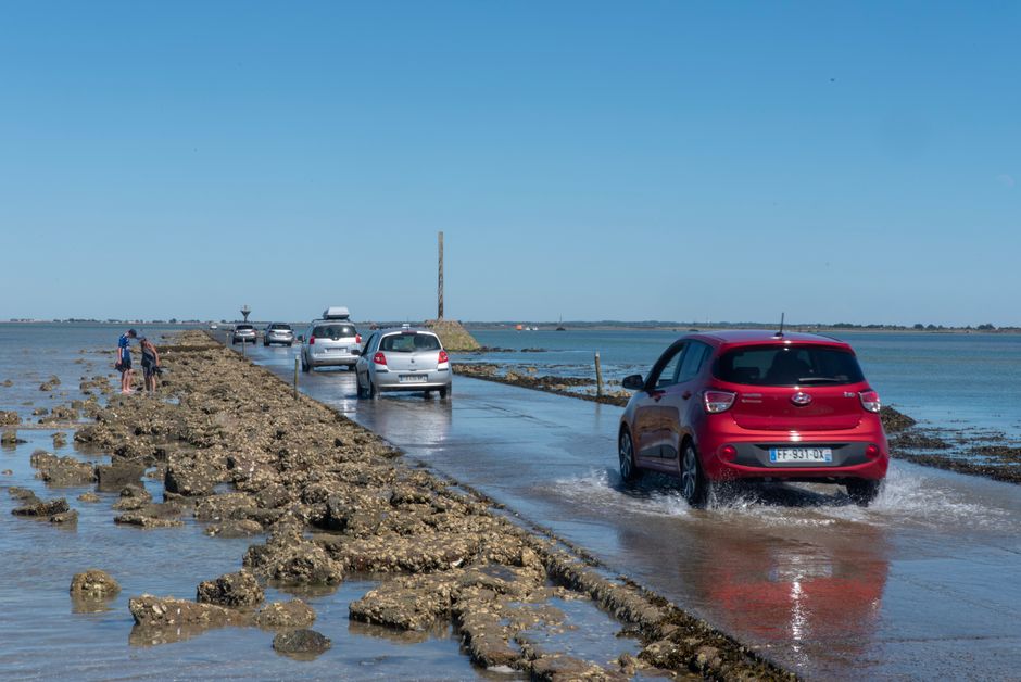 Vehicles driving on the tidal road in Beauvoir-sur-Mer, France during a sunny day.