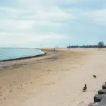 An empty beach meets the ocean under a cloudy sky
