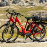 Two vibrant red electric bicycles parked outdoors on a sunny day, scenic backdrop.