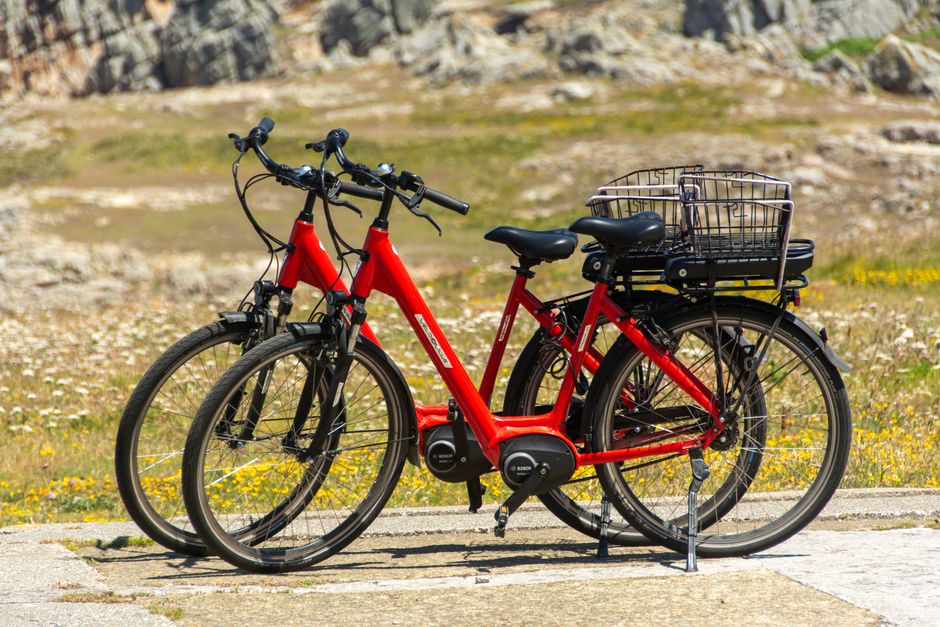 Two vibrant red electric bicycles parked outdoors on a sunny day, scenic backdrop.